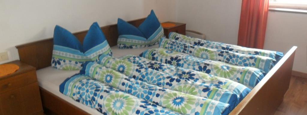 A cozy bedroom with a large double bed and colorful bedspreads. The walls are light and the room has warm lighting conditions. - Appt. Garni Anny - Vent
