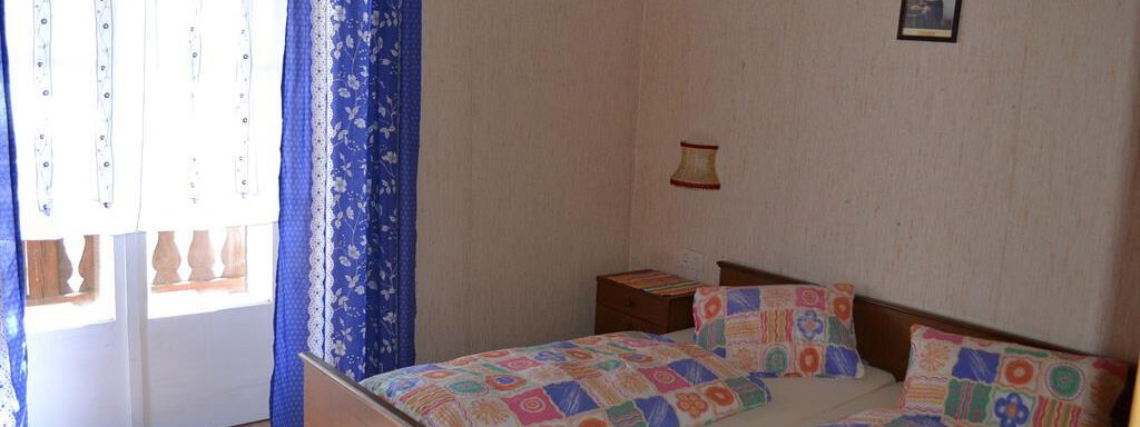 A simple bedroom with two single beds and colorful bedspreads. The room has curtains and a small table next to a window. - Appt. Garni Anny - Vent
