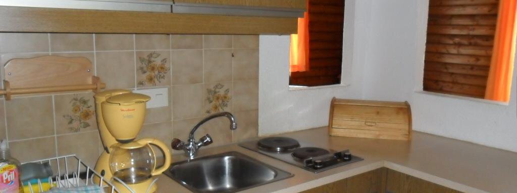 A bright kitchen with wooden cabinets and a small sink. On the countertop, there is a kettle and a rack for dishes. - Appt. Garni Anny - Vent