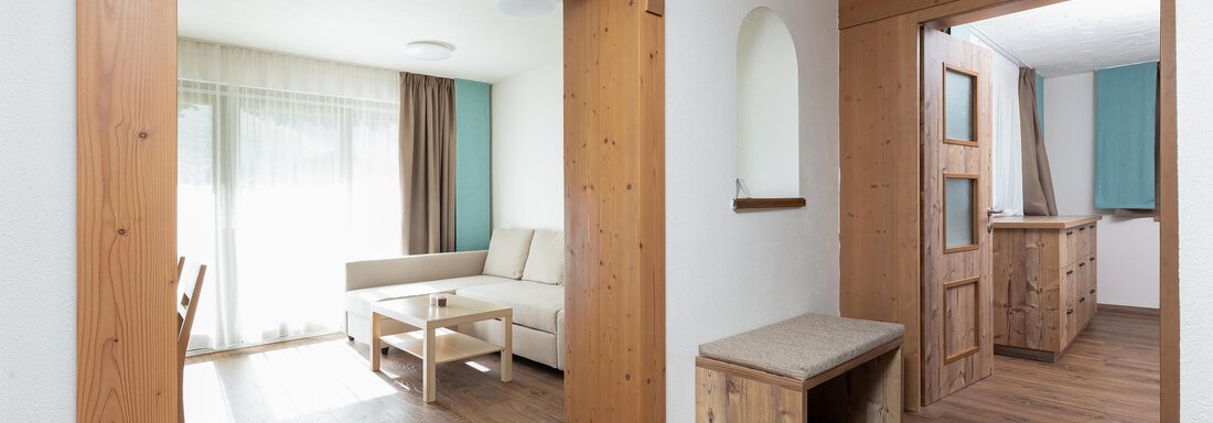 A bright living room with a comfortable sofa and a small table. The room has large windows and natural wood details. - Garni Stefani - Vent