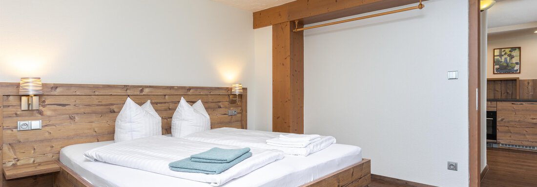 A cozy bedroom with a large wooden bed and white bedding. There is a warm wooden floor and a simple, appealing decor. - Garni Stefani - Vent