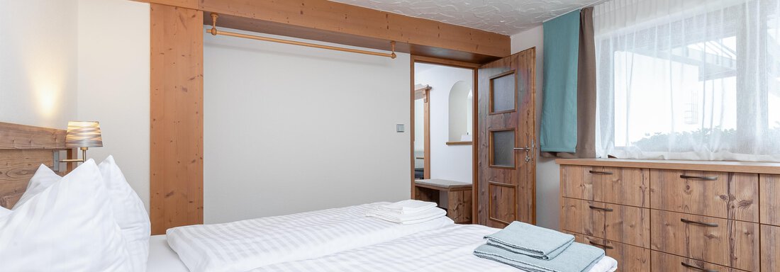 A cozy bedroom with a double bed and wooden decor. There is a wardrobe and plenty of daylight through the window. - Garni Stefani - Vent
