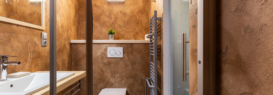 A modern bathroom with warm earth tones. It features a sink, a toilet, and a shower. - Garni Stefani - Vent