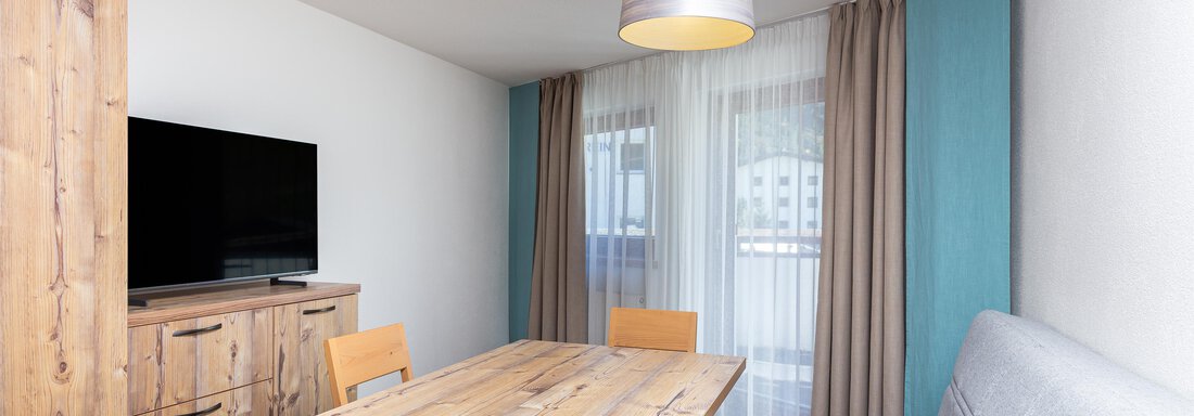 A cozy living space with a wooden table and chairs. A large window front ensures plenty of light. - Garni Stefani - Vent