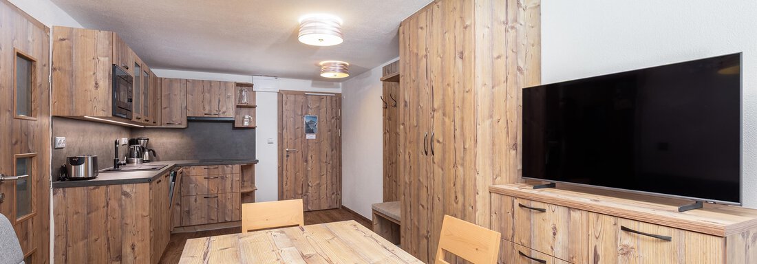 A bright kitchen and living area with wooden furniture. A dining table and a television are also visible. - Garni Stefani - Vent