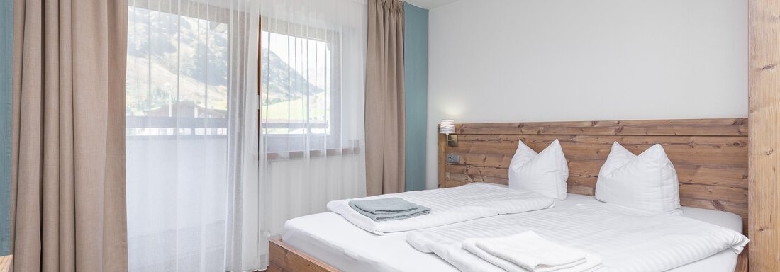 A modern bedroom with a double bed and a warm wood look. Large windows provide plenty of natural light. - Garni Stefani - Vent