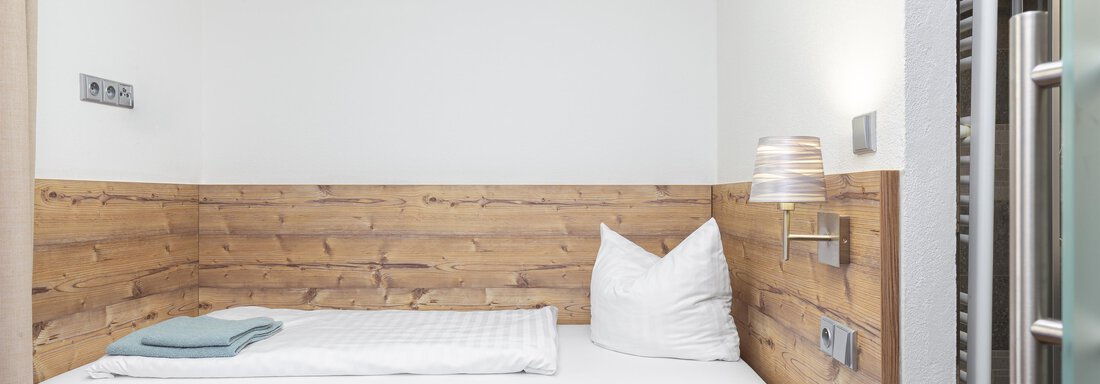 A cozy room with a single bed and wooden paneling. There is a nightstand and a window that lets in a lot of light. - Garni Stefani - Vent