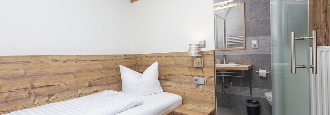 A modern room with wood paneling and a cozy bed. The bathroom is separated by a glass door and is nicely decorated. - Garni Stefani - Vent