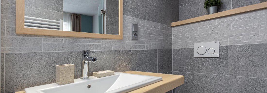 A modern bathroom with gray tiles and a wooden vanity. The mirror reflects the simple and elegant design. - Garni Stefani - Vent