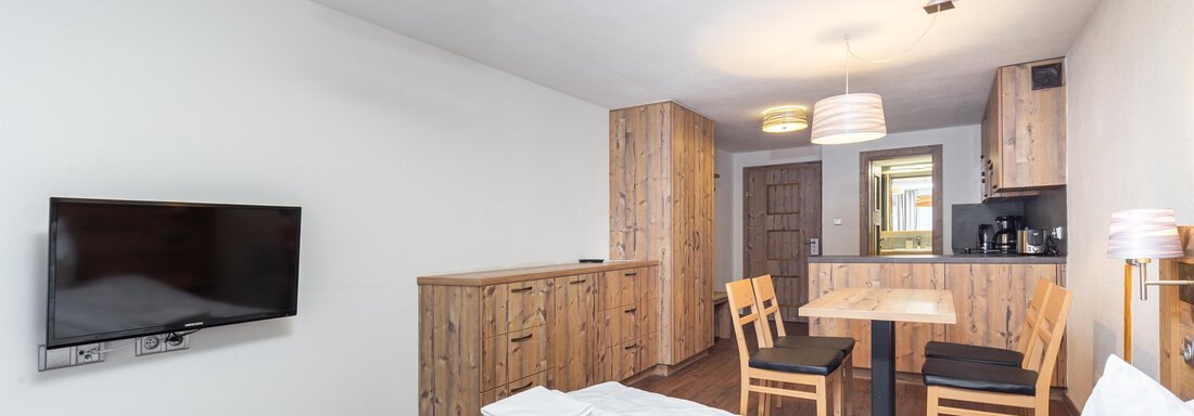 A cozy room with a double bed, a television, and a small dining area. The wooden furniture creates a warm atmosphere. - Garni Stefani - Vent