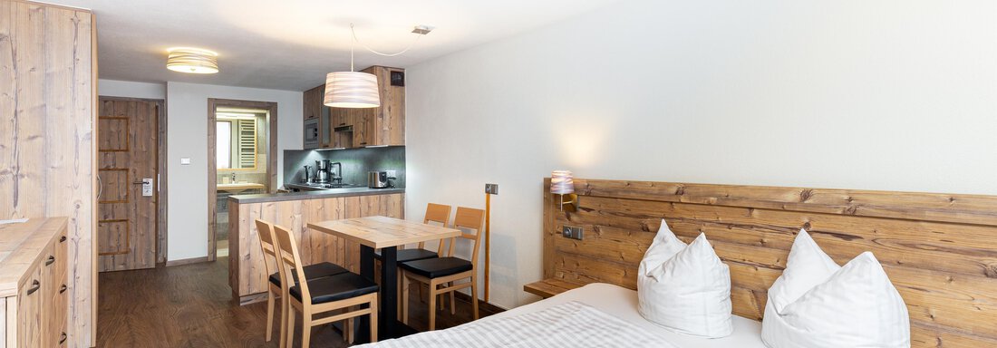 A cozy room with a double bed and two pillows. There is a small dining area and a kitchenette in the background. - Garni Stefani - Vent