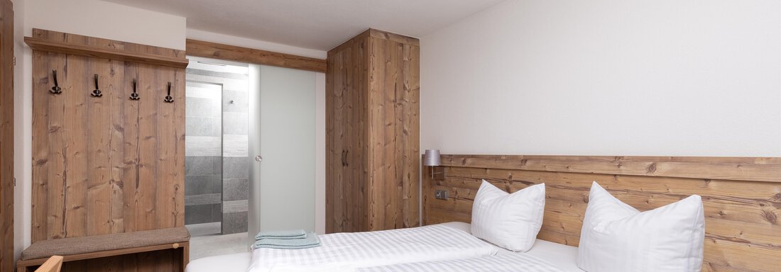 A cozy bedroom with a double bed and white pillows. There are wooden furniture and a view of a bathroom. - Garni Stefani - Vent