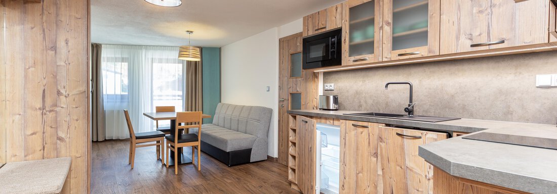 A modern kitchen unit made of wood with a dining area and a cozy seating corner. The room is designed to be bright and welcoming. - Garni Stefani - Vent