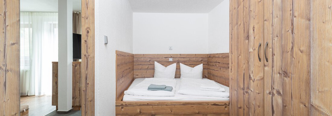 A cozy bedroom with a wooden bed and two pillows. The walls are light, and the room has a modern, minimalist look. - Garni Stefani - Vent