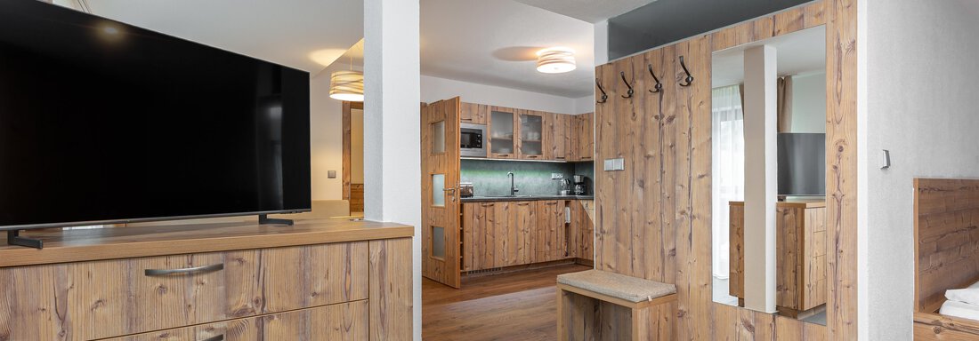 A modern room with wooden furniture and a large television. The open kitchen is well-equipped and creates a warm atmosphere. - Garni Stefani - Vent