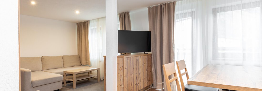 A modern living and dining room with a comfortable couch and dining table. Large windows provide plenty of daylight. - Garni Stefani - Vent