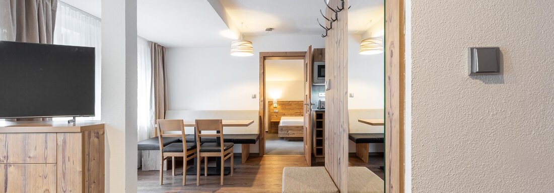 A modern apartment with wooden furniture and a large television. The room is bright and well-structured, with a view of a sleeping area. - Garni Stefani - Vent