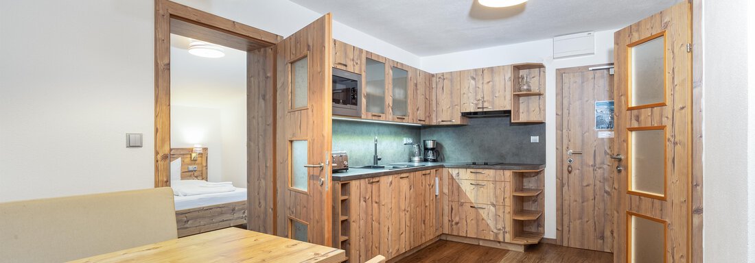 A modern kitchen made of wood with a dining table and chairs. In the background, doors to the bedrooms can be seen. - Garni Stefani - Vent