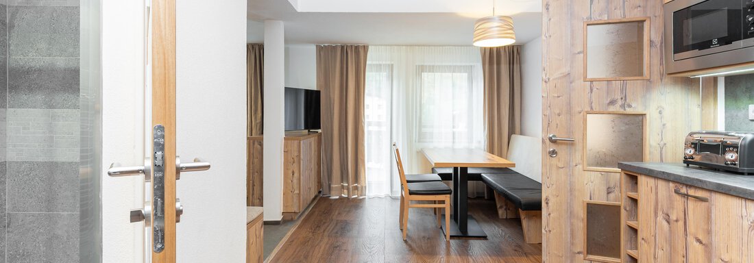 A modern apartment with wood decor and an open living area. In the background, a table, chairs, and a kitchenette are visible. - Garni Stefani - Vent