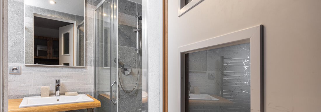 A modern bathroom with a large shower and a wooden vanity. The walls are in neutral colors, and a mirror reflects the light. - Garni Stefani - Vent