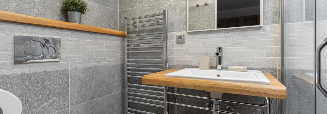 A modern bathroom with gray tiles and a stylish wooden countertop. The space is well-lit and features a towel rack as well as a large mirror. - Garni Stefani - Vent