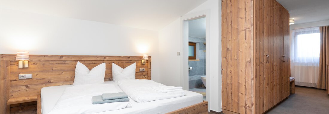 A modern bedroom with wooden details and a large bed. The walls are light, and the room feels welcoming and friendly. - Garni Stefani - Vent