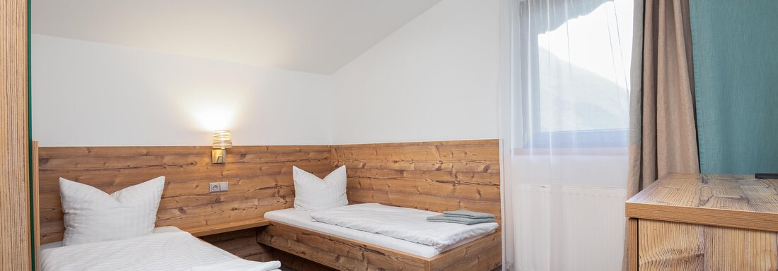 A cozy room with two single beds and wooden paneling. Large windows provide plenty of daylight. - Garni Stefani - Vent