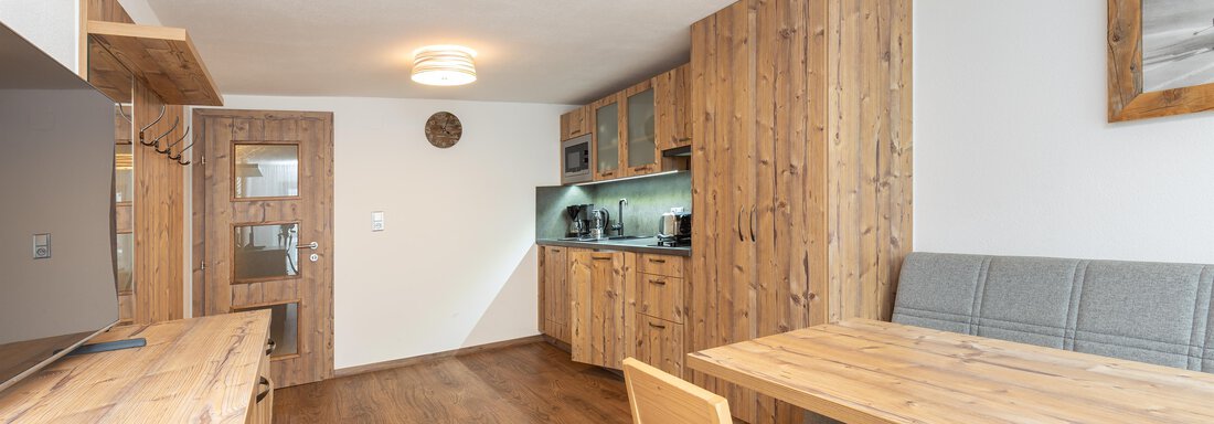 A modern kitchen with wooden details and a bright room. Six chairs are at the table, and the kitchen unit is well equipped. - Garni Stefani - Vent