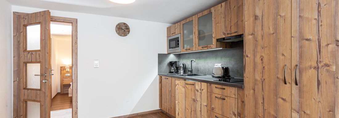 A modern kitchen with wooden cabinets and sleek appliances. The room has a warm floor covering and good lighting. - Garni Stefani - Vent