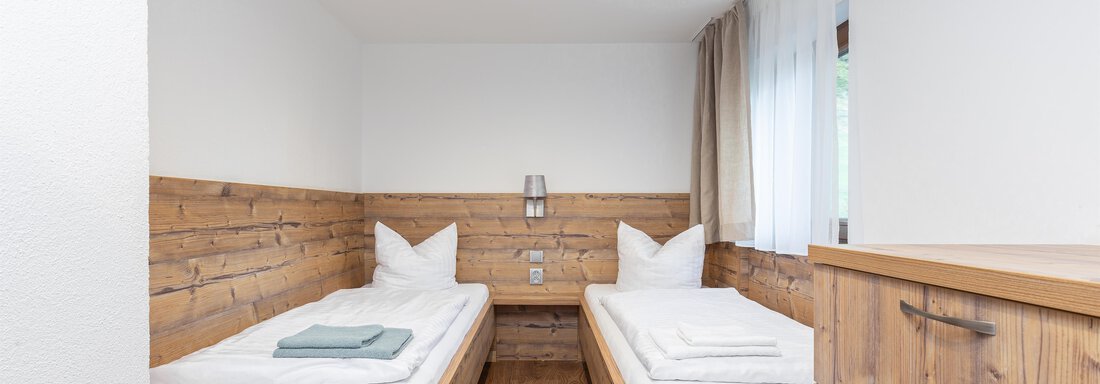 A bright bedroom with two wooden single beds. The walls are partially clad in wood, and there is a modern wardrobe. - Garni Stefani - Vent