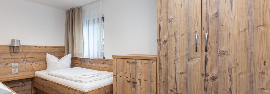 A cozy room with wooden furniture and a bed. Large windows let in plenty of natural light. - Garni Stefani - Vent