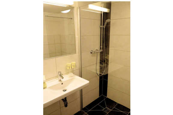 A modern bathroom with a shower and a sink. The walls are clearly tiled and the furnishings are simple and functional. - Gästehaus Soldanella - Vent