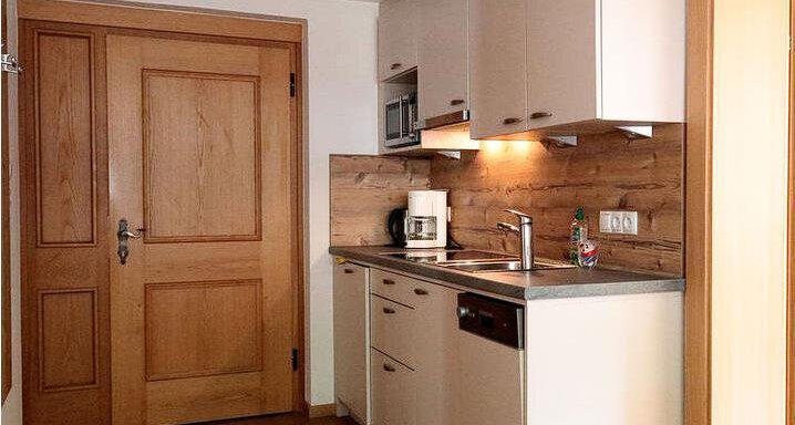 A modern kitchen with bright furniture and wooden paneling. The door in the background leads to another room. - Gästehaus Soldanella - Vent