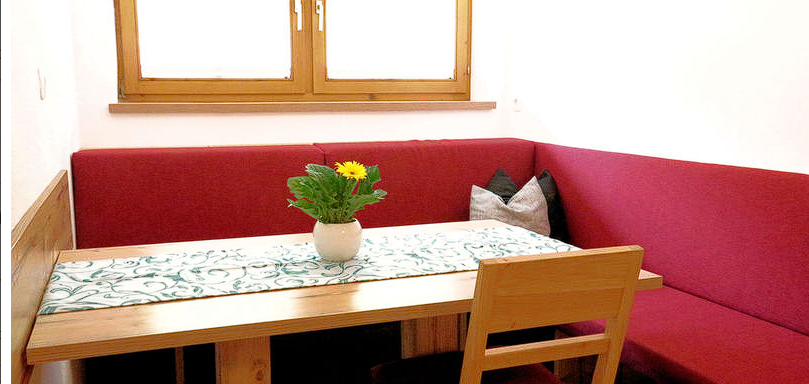 A cozy dining area with a wooden table and red benches. On the table, there is a plant that creates a friendly atmosphere. - Gästehaus Soldanella - Vent