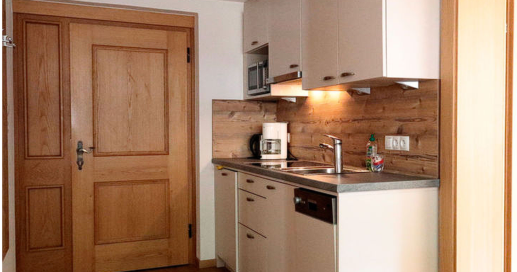A modern kitchenette with wood details, a stove, and a sink. The bright walls and floor create a friendly atmosphere. - Gästehaus Soldanella - Vent