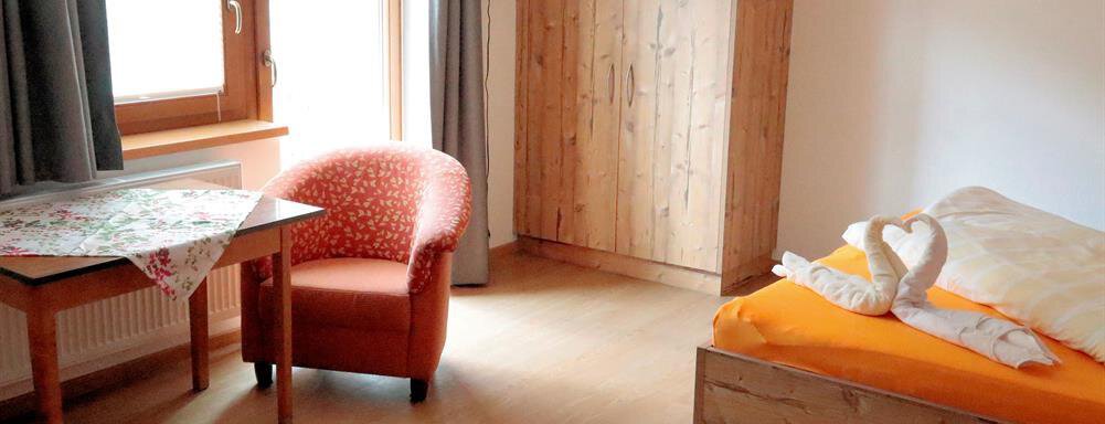 Appartementzimmer1 A cozy room with wood paneling. There is a bed, an armchair, and large windows that let in plenty of light. - Gästehaus Soldanella - Vent