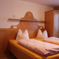 A cozy bedroom with wooden furniture and two beds. The walls are light and there are large pillows on the beds. - Gästehaus Soldanella - Vent