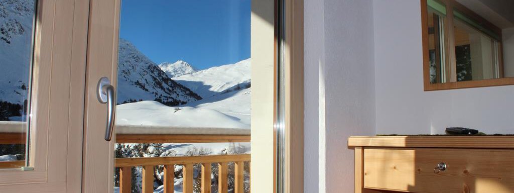 A room with a view of snow-covered mountains and a clear blue sky. The balcony door opens to a breathtaking winter landscape. - Gästehaus Soldanella - Vent