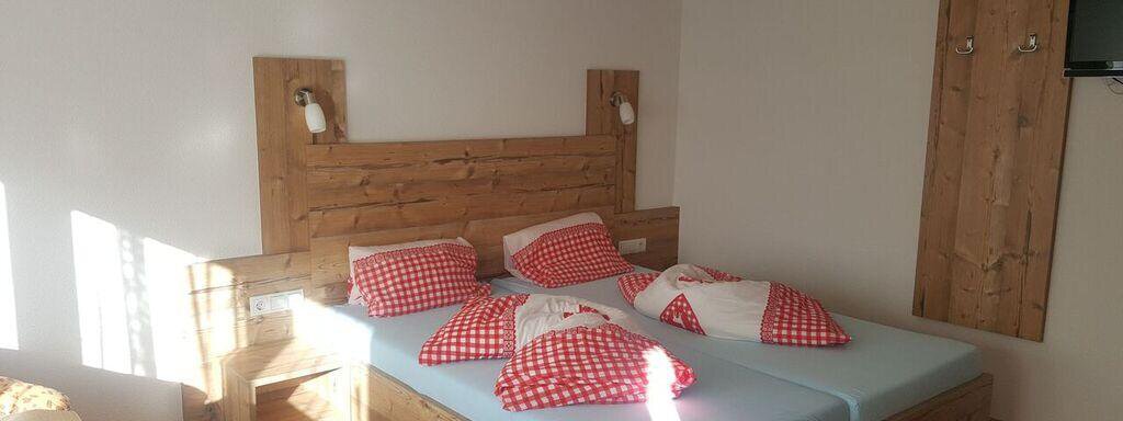 A cozy room with a double bed and red-and-white pillows. A TV is hanging on the wall, and the room is bright and friendly. - Gästehaus Soldanella - Vent
