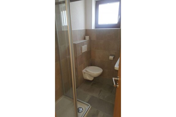 A modern bathroom with a shower cubicle and a toilet. Bright tiles and a window create a friendly atmosphere. - Gästehaus Soldanella - Vent
