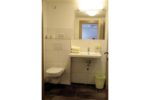 A modern bathroom with a white toilet and a sink. Towels are neatly arranged on the sink, and a mirror reflects the room. - Gästehaus Soldanella - Vent