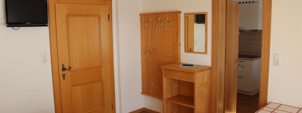 IMG_0676 A cozy room with light wooden furniture and a TV on the wall. There is a small table and access to a kitchen through the indicated door. - Gästehaus Soldanella - Vent