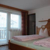 A cozy bedroom with two beds and a balcony door. The room has light curtains and a wooden ceiling. - Gästehaus Soldanella - Vent