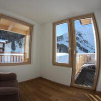 A bright room with large windows and a view of snow-covered mountains. The floor is made of wood, and the room feels cozy. - Gästehaus Soldanella - Vent