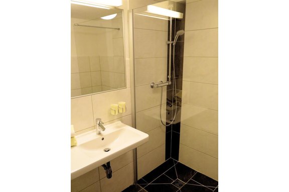A modern bathroom with a shower and a sink. The walls are light tiled, and there are some toiletries on the sink. - Gästehaus Soldanella - Vent