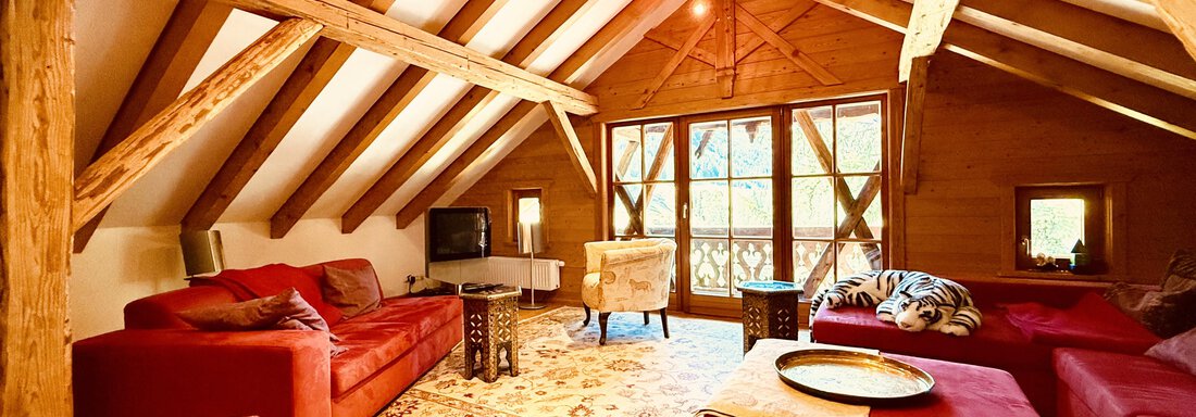 A cozy living room in the attic with red sofas and a wooden floor. Large windows provide plenty of daylight and a view of the outdoors. - Haus Freistabl - Vent