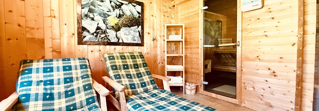 A cozy sauna cabin with wooden cladding and two loungers. In the background, a sauna door and a beautiful picture on the wall can be seen. - Haus Freistabl - Vent