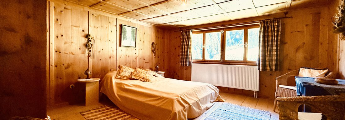 A cozy bedroom with wood paneling and plenty of natural light. The room is simply furnished and has a warm, inviting atmosphere. - Haus Freistabl - Vent