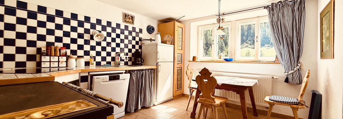 A cozy kitchen with blue and white tiles and a dining table. The room is brightly lit and has windows with a view to the outside. - Haus Freistabl - Vent