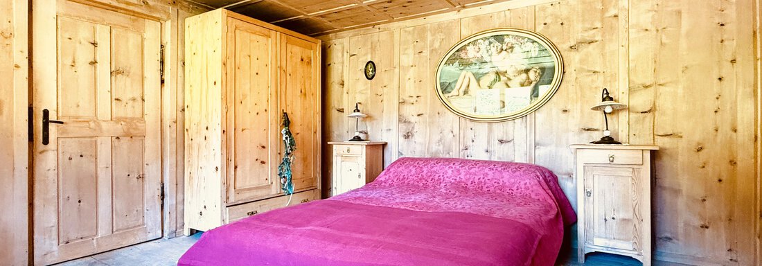 A cozy bedroom with wood paneling and a large bed in pink. The room has a rustic design and warm lighting that creates an inviting atmosphere. - Haus Freistabl - Vent